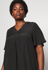 Vestido preto de mangas curtas com decote em V, apresentando uma silhueta fluida e uma textura subtil ao longo do corpo.