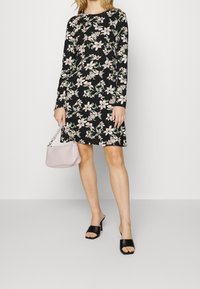 Blommig svart klänning med långa ärmar, med ett mönster av vita och rosa blommor. Kombinerad med en ljusrosa handväska och svarta öppna klackar.