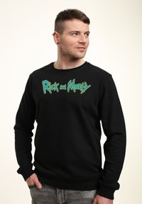 Felpa nera con il logo di "Rick and Morty" in caratteri vibranti verde e blu, colletto rotondo e maniche lunghe. Tessuto morbido e liscio.