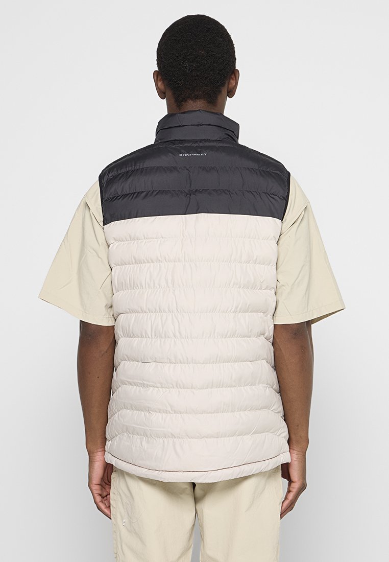 Uomo che indossa un gilet imbottito leggero beige e nero con la scritta "OMNI-HEAT" sulla parte superiore della schiena, camicia a maniche corte beige e pantaloni beige, vista da dietro.