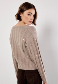 Suéter de punto beige con rayas verticales y pequeños patrones de corazones blancos, con corte relajado y dobladillo acanalado, visto desde la parte posterior.