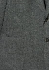 Grauer Blazerstoff mit Struktur, versehen mit einer aufgesetzten Tasche und zwei dunklen Knöpfen. Das Material zeigt ein dezentes Webmuster und eine glatte Oberfläche.