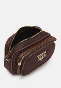 Hnědá prošívaná syntetická taška přes rameno se zlatými zipy, dvěma přihrádky a trojúhelníkovým logo akcentem vepředu.