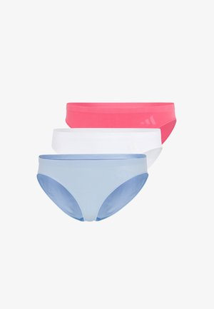 Frau mit langen Zöpfen steht barfuß und trägt ein hellblaues Sport-BH und passende Bikini-Unterwäsche vor weißem Hintergrund.