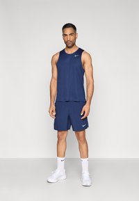 Marineblaues sportliches Tanktop und Shorts aus leichtem Stoff. Verfügt über ein kleines weißes Nike-Logo. Kombiniert mit weißen Socken und Turnschuhen.