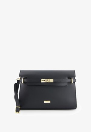 Sac à main en cuir noir avec un design structuré, quincaillerie dorée, fermeture rabat en haut et une bandoulière amovible. Étiquette visible à l’avant.