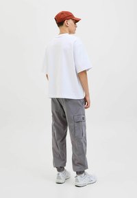 Weißes übergroßes T-Shirt, graue Cargo-Hosen mit Seitentaschen und weiße Sneaker. Braune Kappe; lässiges Design mit elastischen Bündchen an den Hosen.
