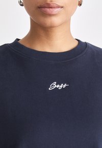 Felpa blu navy con collo a costine, caratterizzata da un logo "Boss" ricamato in bianco sul petto. Tessuto morbido con una texture liscia.
