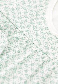 Witte stof met een lichtgroen bloemenpatroon, voorzien van plooien en een ronde halslijn met een gestructureerde afwerking.