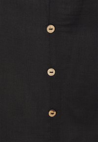 Tissu noir avec une finition texturée présentant cinq boutons en bois alignés au centre. Les boutons sont ronds avec une fente horizontale unique.