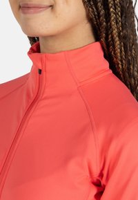 Lätt, korallfärgad zip-up-jacka med hög krage. Slät yta och platta sömmar, utformad för komfort och funktionalitet.