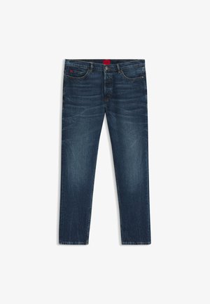 Tumedat sinised teksad sirge säärega, millel on pleekinud alad, viie tasku disain ja punane logo silt vöökohtadel.