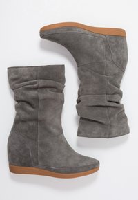 Stivali a zeppa grigi in suede con un design superiore morbido, caratterizzati da una texture liscia e una suola in gomma marrone.