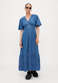 Denim maxi-kjole med V-hals, korte ermer, frontlukking med knapper og lagdelt kant. Har lyseblåt stoff med subtil tekstur.