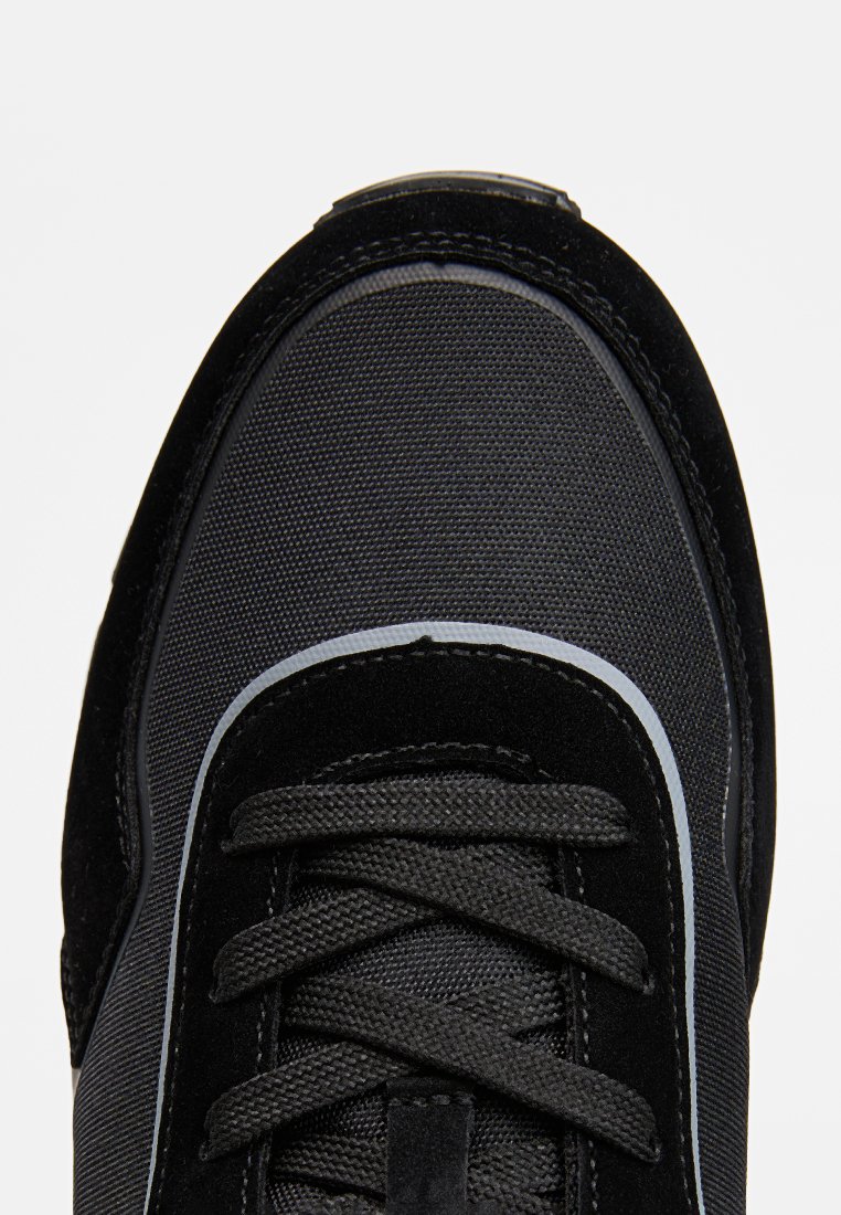 Czarne zamszowe i siateczkowe sneakersy z okrągłymi sznurówkami, teksturowanym czubkiem i smukłą konstrukcją z szarymi akcentami wzdłuż brzegów.