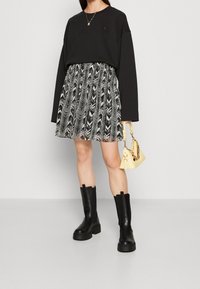 Sweatshirt noir oversize, jupe à volants noir et blanc à motifs, sac à main jaune et bottes noires imposantes. Matériaux lisses et texturés.