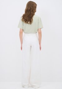 Lichtgroen t-shirt met korte mouwen gecombineerd met hoge taille, vloeiende witte broek, die een losse pasvorm en een gladde stofstructuur benadrukt.