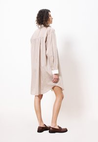 Gestreiftes Hemdkleid in hellbeige mit blauen und orangenen Streifen, mit langen Ärmeln und einem geschwungenen Saum, kombiniert mit braunen Schlupfschuhen.