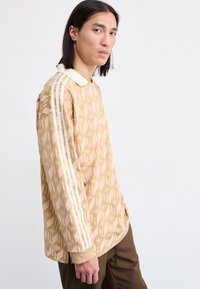 Long-sleeve tan patterned pullover with a white collar and three white stripes down the sleeves; features an abstract design.