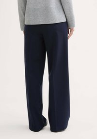 Pantalons navy à jambes larges, en tissu lisse, avec une taille haute et un design classique, associés à un pull en tricot gris clair.