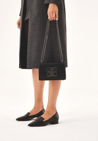 Borsa a tracolla in pelle nera con catena, caratterizzata da un design geometrico impresso sul davanti. Abbinata a ballerine nere.