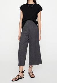 Czarny bawełniany t-shirt z podwiniętymi rękawami w połączeniu z szerokimi, szarymi spodniami o teksturowanej powierzchni oraz czarnymi sandałami na paseczkach. Prosty i minimalistyczny design.