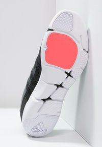 Mustan urheilukengän pohja, jossa on valkoinen välikerros. Sisältää vaaleanpunaisen kumikorosteen ja tekstuuripinnan paremman pidon vuoksi. Adidas-logo näkyvissä.