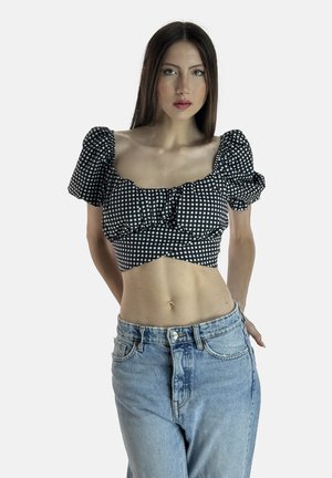 Top corto a scacchi in bianco e nero con maniche a sbuffo, frontale gather, abbinato a jeans azzurri a vita alta, che mostrano un design aderente.