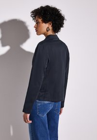 Svart, åtsittande jacka med en elegant design och krage, i kombination med blå vida jeans. Har långa ärmar och en mjuk textur.