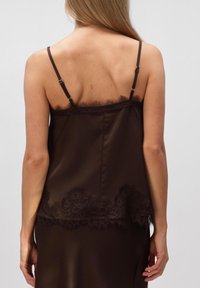 Camisole en satin marron avec bretelles ajustables, ornée d'une bordure en dentelle en haut et d'accents délicats en dentelle au niveau de l'ourlet. Texture lisse.