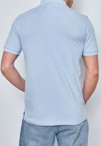 Polo shirt bleu clair, à manches courtes, en mélange de coton, avec un col tricot plat, vue de dos, texture lisse et sans motifs visibles.