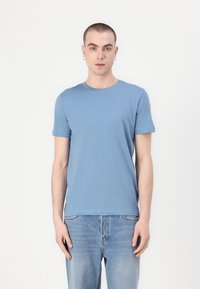 Μπλε βαμβακερή μπλούζα με κοντά μανίκια, στρογγυλή λαιμόκοψη και στενή εφαρμογή, συνδυασμένη με τζιν ελαφριάς πλύσης. Μινιμαλιστικός σχεδιασμός.