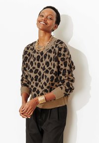 Pull à imprimé léopard marron et noir, en tissu tricoté, col rond, ourlet et poignets côtelés. Porté avec un pantalon plissé noir et des accessoires dorés.