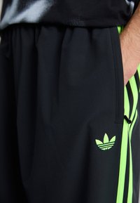 Melnas sporta šortas ar zaļām svītrām un Adidas logotipu. Izgatavotas no gludas materiāla, ar sānu kabatu un elastīgu jostasvietu.
