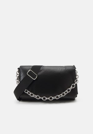 Pochette en cuir noir avec une large bandoulière en tissu réglable et une poignée décorative en chaîne argentée sur un fond uni.