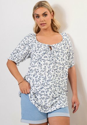 Witte bloeiende blouse met blauwe patronen, korte puffmouwen en een vierkante halslijn. Gepaard met lichtblauwe denim shorts.