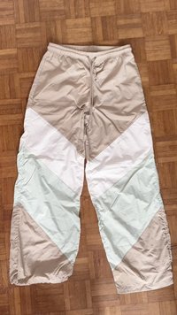 Pantalones deportivos ligeros y multicolores que presentan una mezcla de paneles en beige, blanco y verde claro en un diseño de chevrón, con cintura elástica.