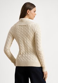 Krēmkrāsas džemperis ar kabeļu adījumā veidotu rakstu, augstu ribotu apkakli un garām piedurknēm. Virsma ir reljefaina ar pacēltiem rakstiem, ar ribotām aprocēm un apakšu.