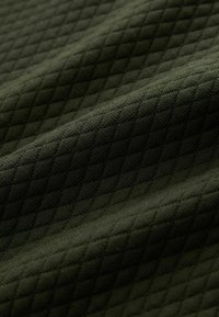 Tejido verde texturizado con un patrón de diamante y un sutil brillo, que muestra una suave textura tejida. Ideal para aplicaciones de ropa o tapicería.