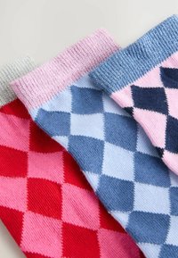 Calze argyle colorate in rosso, rosa, blu e grigio. Presentano polsini a coste e una texture morbida. Ogni calza ha motivi geometrici distintivi.