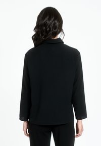 Juodas švarkas su pritaikytu dizainu. Pasižymi ilgomis rankovėmis ir lygia tekstūra, papildyta klasikinėmis apykaklėmis ir subtiliais siuvinėjimo detalėmis.