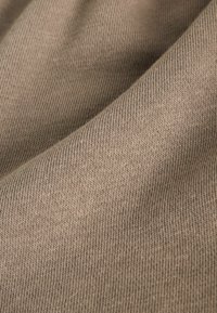Beige ribbet stof med en blød tekstur og en let skinnende overflade, prydet med jævnt fordelte strikmønstre og en blød fald.