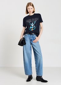 T-shirt grafica blu navy con design dei Pink Floyd, abbinata a jeans larghi di colore blu chiaro e ankle boots neri col tacco. Clutch nera tenuta in una mano.