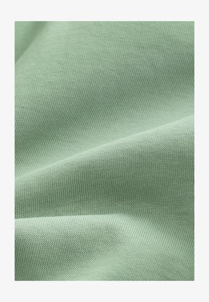 Jasnozielona tkanina o gładkiej, lekko teksturowanej powierzchni i drobnym prążkowanym wzorze, złożona w łagodne zakrzywienia i miękko opadająca.