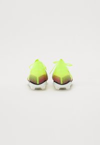 Neon gule fodboldstøvler med en struktureret overdel, gradient røde og sorte accenter samt hvide såler. Tied laces på bagsiden fremhæver designet.