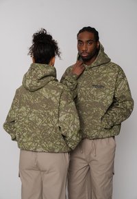 Sweat-shirts à capuche à motif camouflage en vert olive avec des accents vert clair et une poche avant. Dotés d'une coupe décontractée et de grandes capuches.