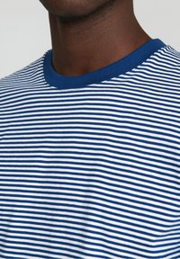 Blau-weiß gestreiftes T-Shirt mit rundem Halsausschnitt. Der Stoff scheint weich und gleichmäßig texturiert zu sein; die Streifen haben eine konsistente Breite.