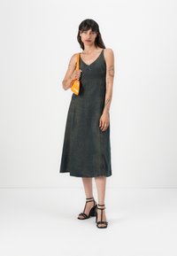 Temno modra denim A-linijska obleka z tankimi naramnicami, s križnim izrezom in detajli gumbov. Ujemajo se z črnimi sandali s trakovi in oranžnim nahrbtnikom.