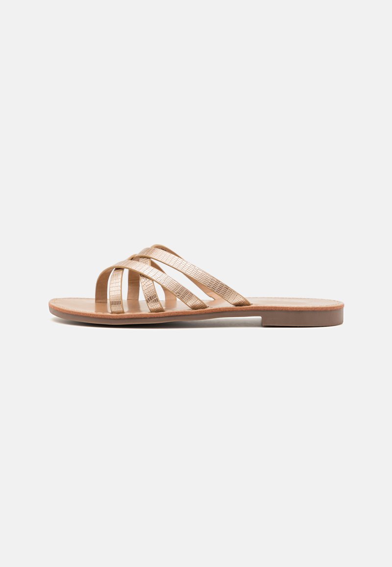 Sandali piatti con una tomaia beige texturizzata che presenta tre cinturini incrociati. La suola è marrone chiaro e ha un design minimalista.
