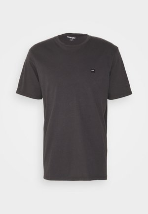 Camiseta de algodón gris oscuro con cuello redondo y mangas cortas. Presenta un pequeño parche de logo negro en el lado izquierdo del pecho.